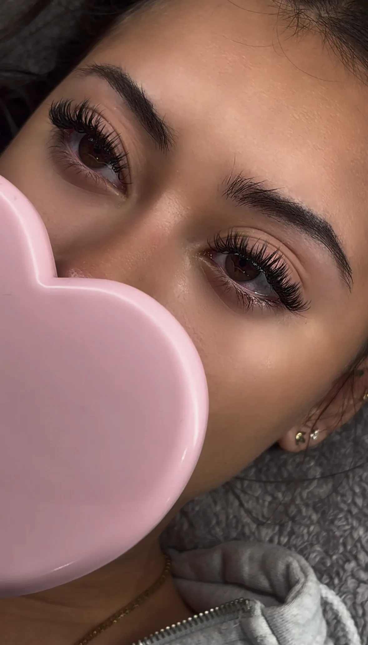 Close-up of a set of lash extensions, with a pink heart mirror held alongside
